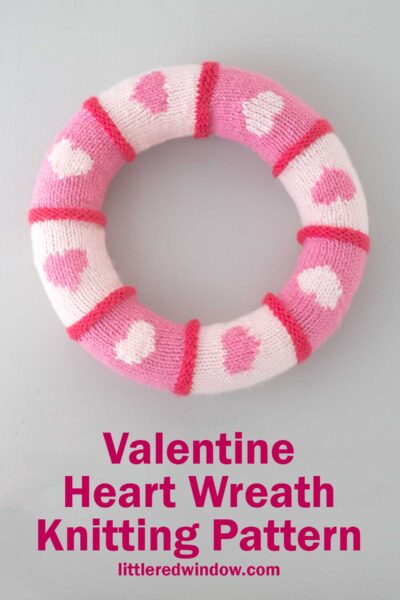A knitted wreath with pink and white stripes and heart patterns. The caption reads "Valentine Heart Wreath Knitting Pattern" with "littleredwindow.com" beneath.