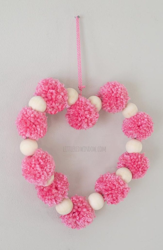 left angle view of heart shape made of pink pom poms and wood beads