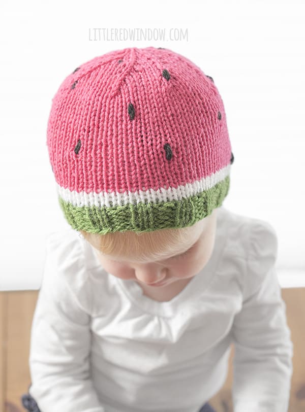 Baby wearing green white and pink knit watermelon hat with black seeds