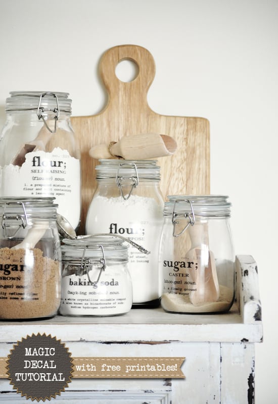 Group of 5 lidded glass jars with labels that have the written definition of each baking ingredient like flour and sugar