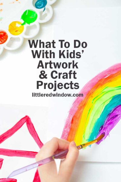 white table with childs hand painting a picture of a rainbow and a house next to a paint palette