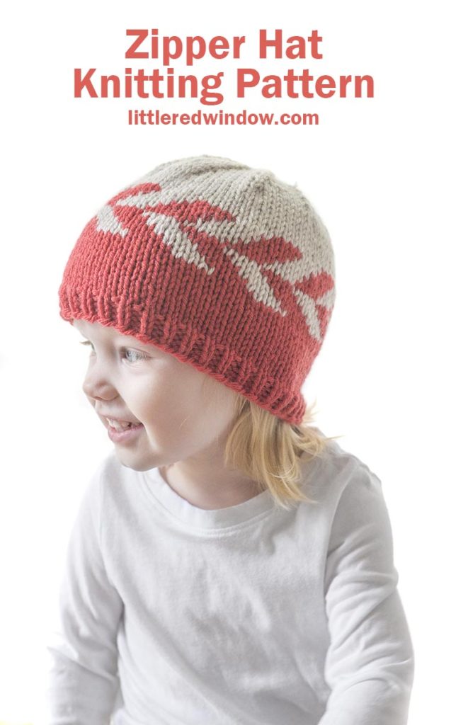 smiling girl in white shirt wearing knit hat with red and tan zipper pattern around the middle looking off to the left