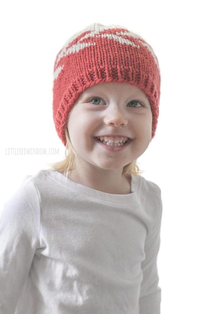 smiling girl wearing red and tan zipper hat looking up above the camera