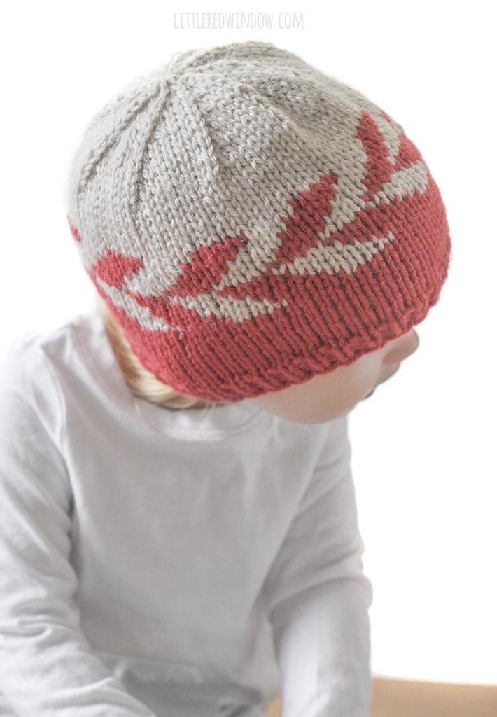 girl in white shirt wearing red and tan knit hat with zipper pattern around the middle looking down over her left shoulder