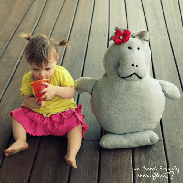 little girl sitting next to large stuffed manatee